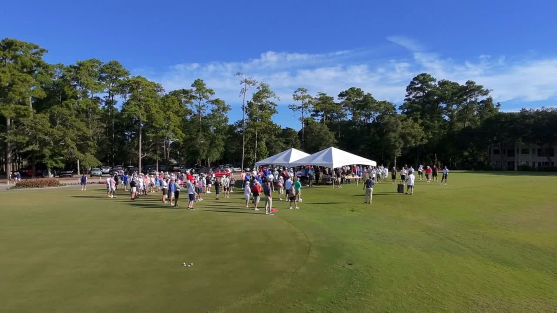 Drone shot of Tidewater Golf Club’s driving range on the morning of the Labor Day Folds of Honor Tournament. Dozens of golfers gather for breakfast and mingle near registration tables while Jake Green, representing Folds of Honor, delivers a speech to the crowd against the scenic backdrop of the course.